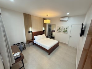 A hotel room with a bed, bedside table, chair, desk, and a television. - Harman Suites Moalboal (Moalboal)