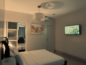 Ein Hotelzimmer mit einem Bett, einem Fernseher, einem Deckenventilator, einer Klimaanlage und einem Bild an der Wand.