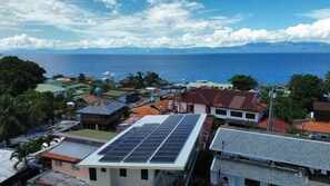 Eine Küstenstadt mit Gebäuden, einige mit Solaranlagen, und Blick auf das Meer und Berge in der Ferne.