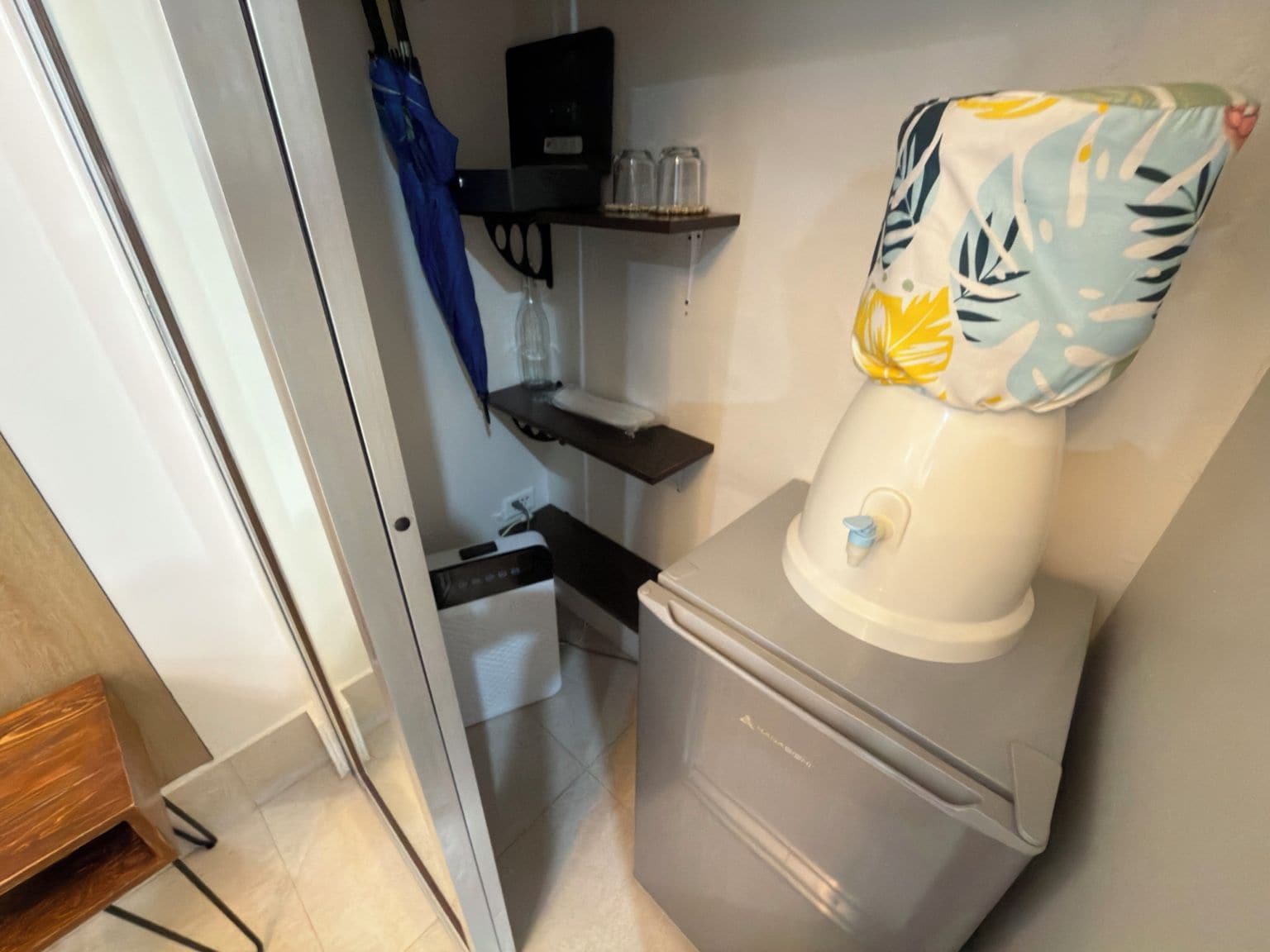Un baño compacto con inodoro, un estante con un filtro de agua y un paraguas azul colgado en la pared.