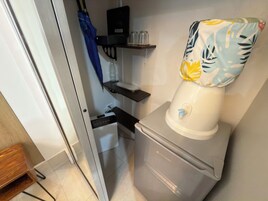 Un baño compacto con inodoro, un estante con un filtro de agua y un paraguas azul colgado en la pared.
