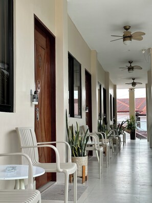Ein Hotelkorridor mit Deckenventilatoren, weißen Plastikstühlen und Topfpflanzen.