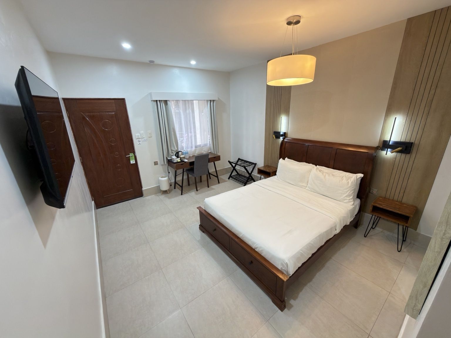 A hotel room with a bed, a desk, a chair, a TV, and a window with curtains.