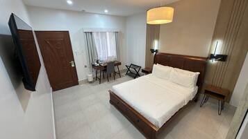 A hotel room with a bed, a desk, a chair, a TV, and a window with curtains.