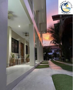 A modern building with a covered outdoor area, a pathway, and a sunset view. - Harman Suites Moalboal (Moalboal)