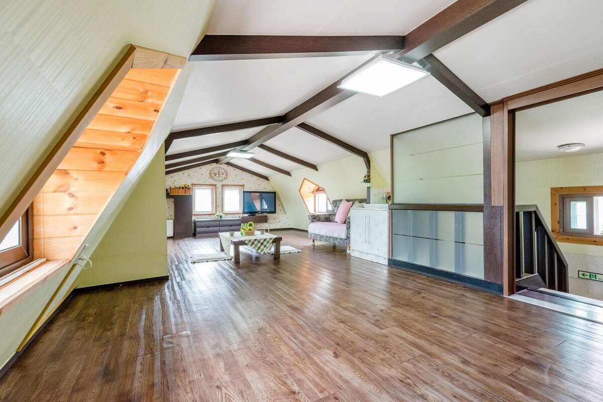 Un loft espacioso con techos altos, vigas de madera a la vista y techo inclinado.