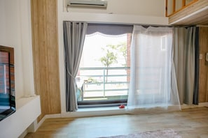 Una habitación con un ventanal grande, suelo de madera, un tapete pequeño y un televisor en la pared izquierda.