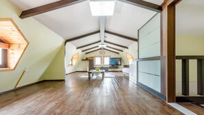 Een ruime zolderkamer met houten vloeren, een schuine kap en een groot raam.