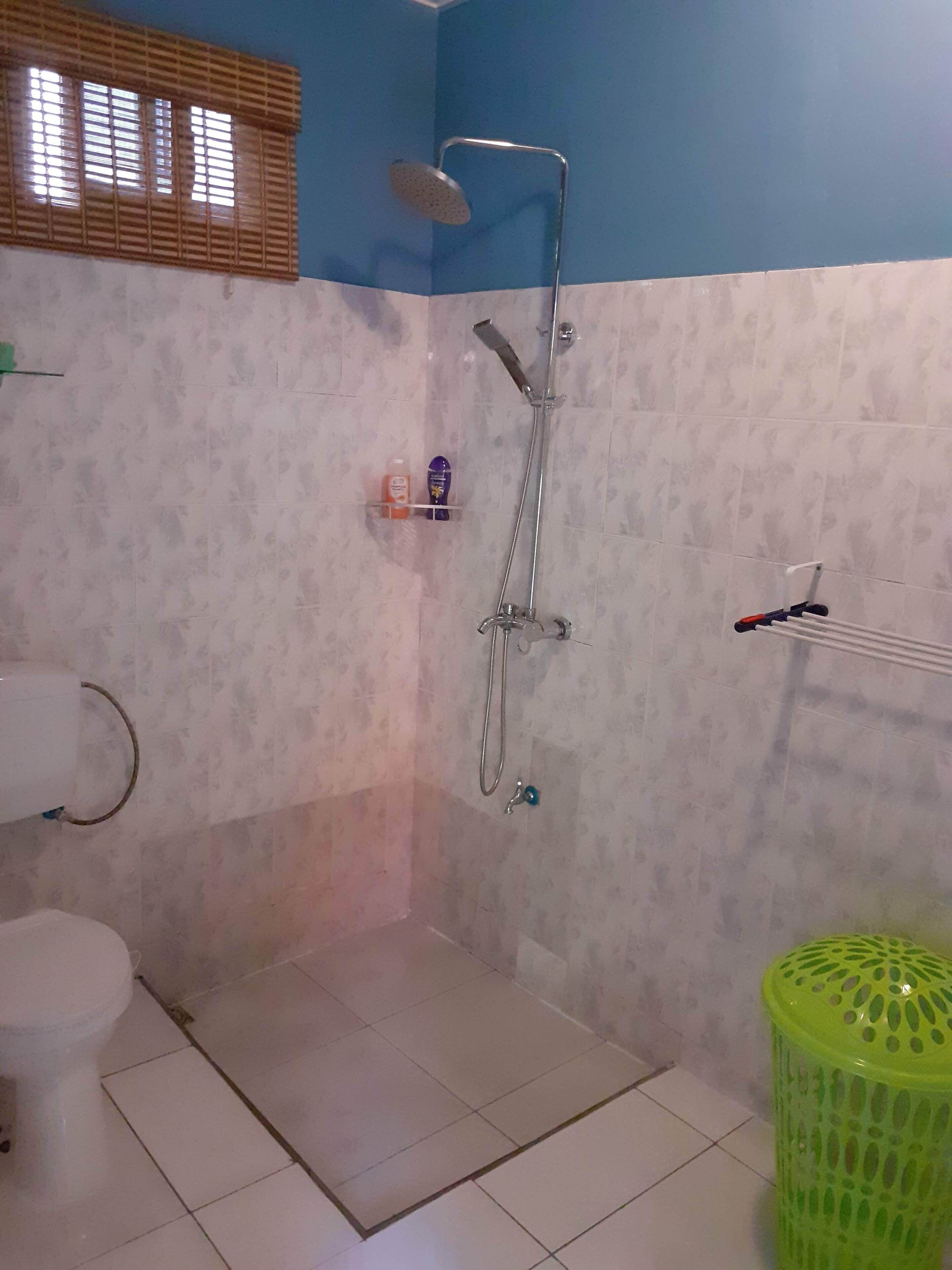 A small bathroom with a shower, toilet, and a green trash bin.