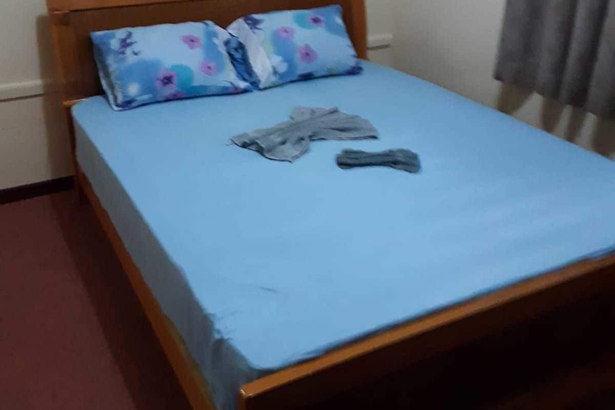 A single bed with a wooden headboard, a floral pillow, and a blue bedspread.