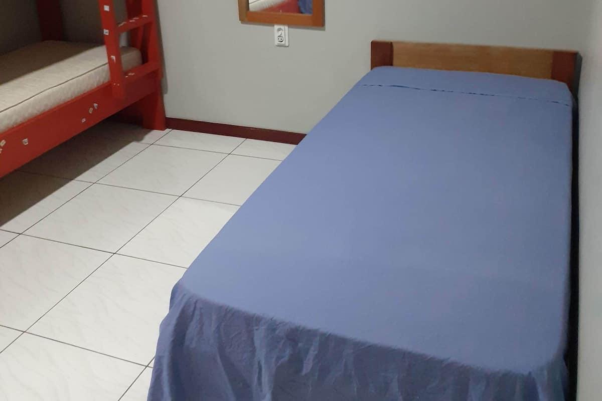 A room with a bunk bed, a single bed, a mirror, and a tiled floor.