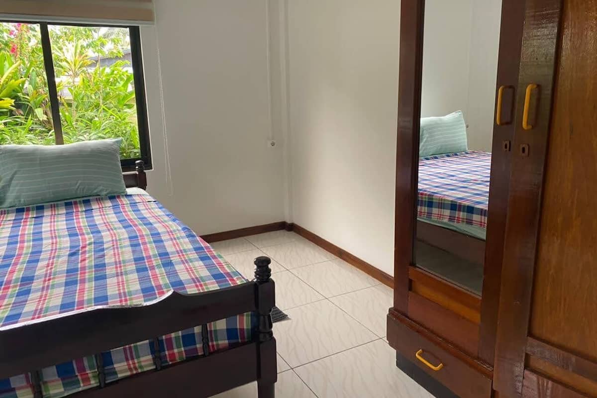 A bedroom with a bed, a wooden wardrobe, and a window with a view of greenery.