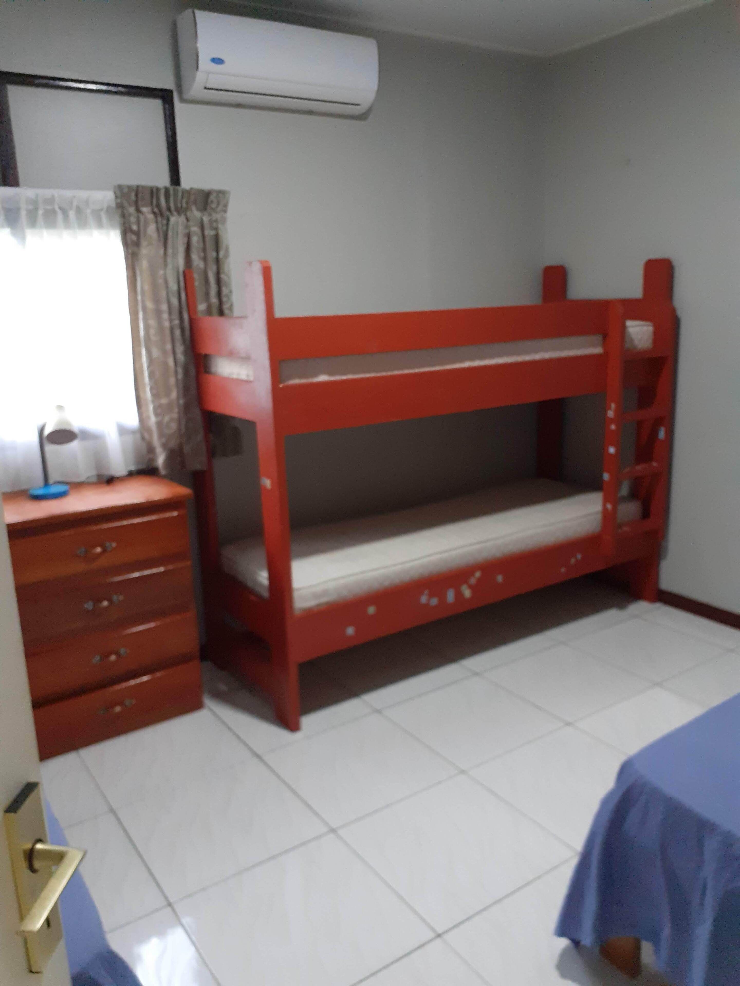 A room with a bunk bed, a dresser, a desk, and an air conditioner.