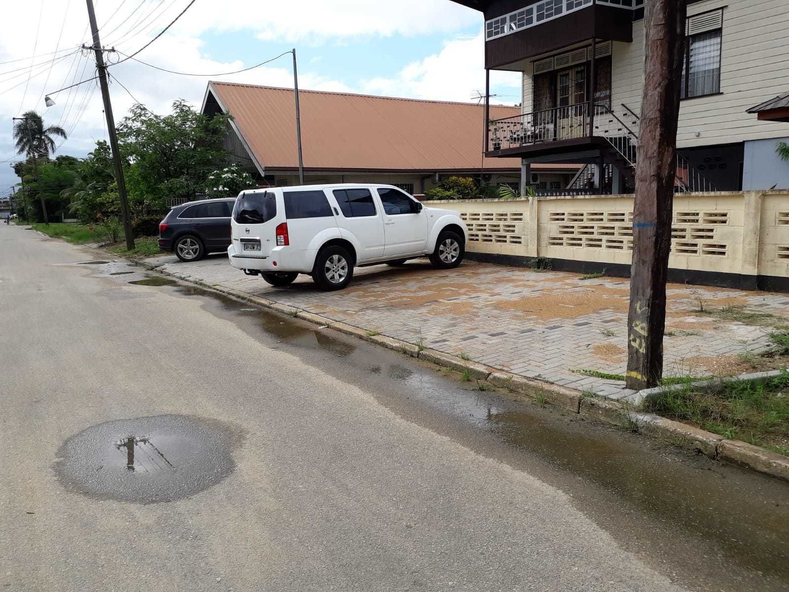 Una calle residencial con una camioneta SUV blanca estacionada en la banquina.