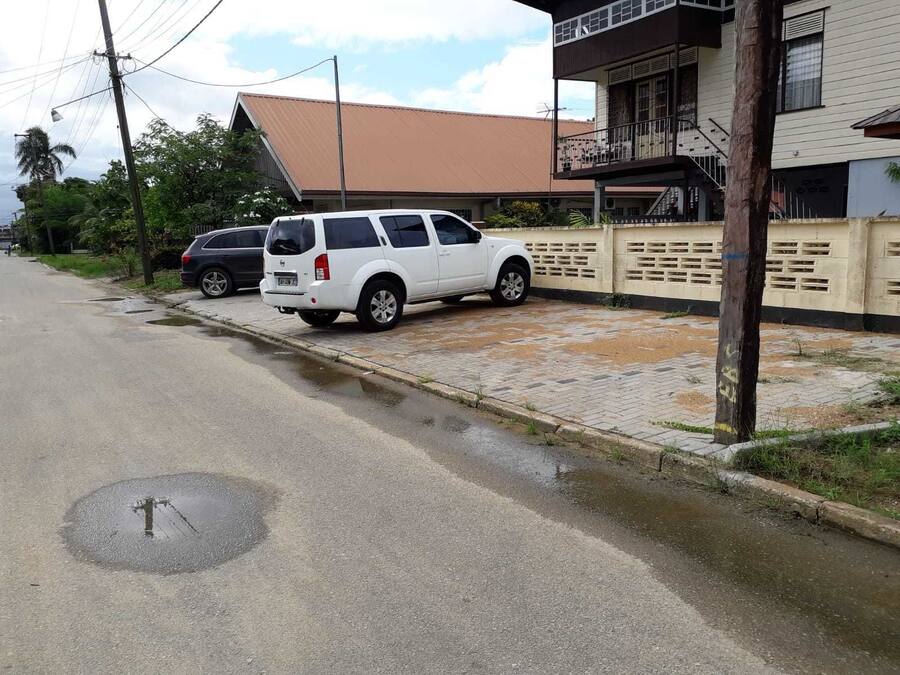 Una calle residencial con una camioneta SUV blanca estacionada en la banquina.