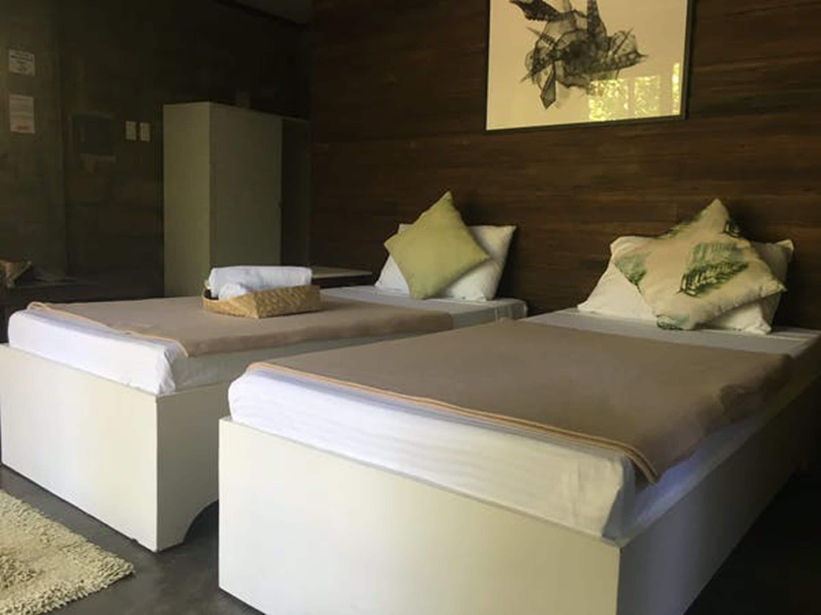 A hotel room with two beds, a large wardrobe, and a framed artwork on the wall.