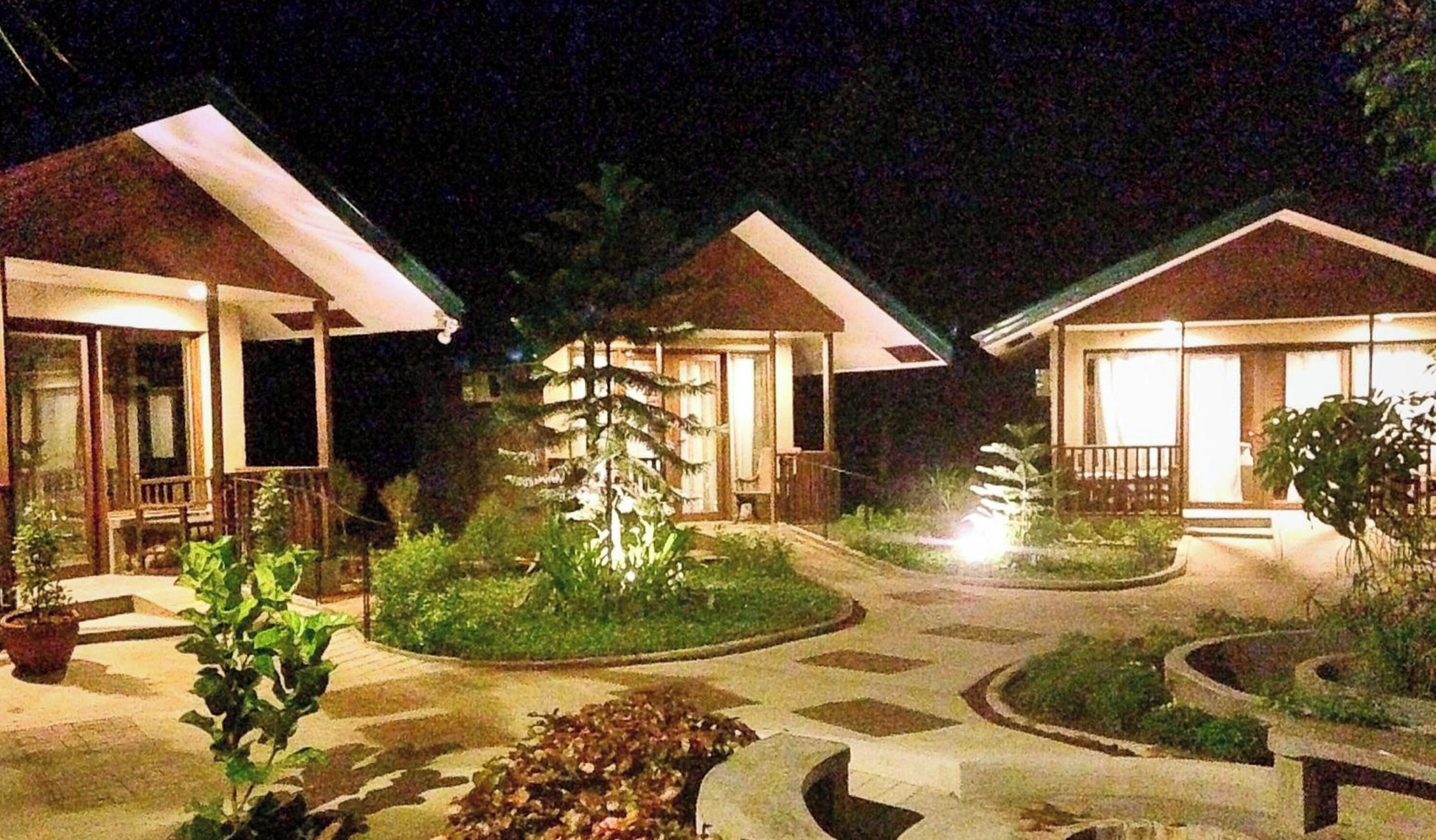 A nighttime view of a resort with multiple bungalow-style buildings, each featuring a porch and a well-lit entrance.