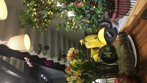 A dining area with a yellow scooter, a wicker chair, and a hanging plant with yellow flowers. - Banana Flower Homestay (Da Nang)