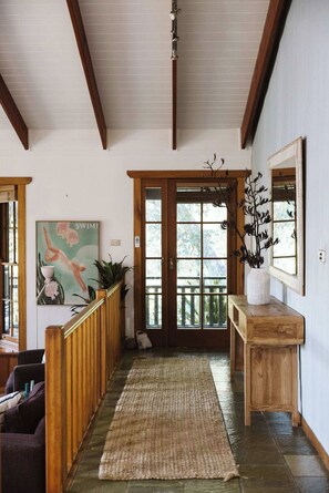A hallway with wooden beams, a wooden bench, a door with glass panels, and a framed picture on the wall.