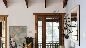 Un couloir avec des poutres en bois, un banc en bois, une porte avec des panneaux de verre et un tableau encadré au mur.