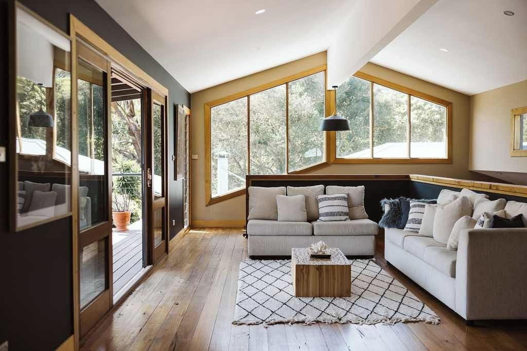 A spacious living room with a large sofa, a coffee table, and a view of the outdoors through large windows.
