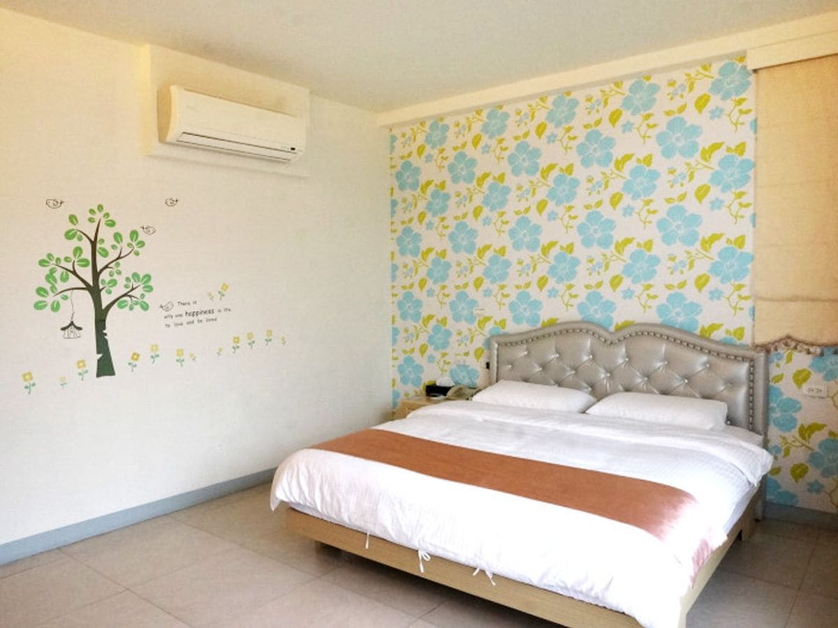 A bedroom with a bed, a wall-mounted air conditioner, and floral wallpaper.