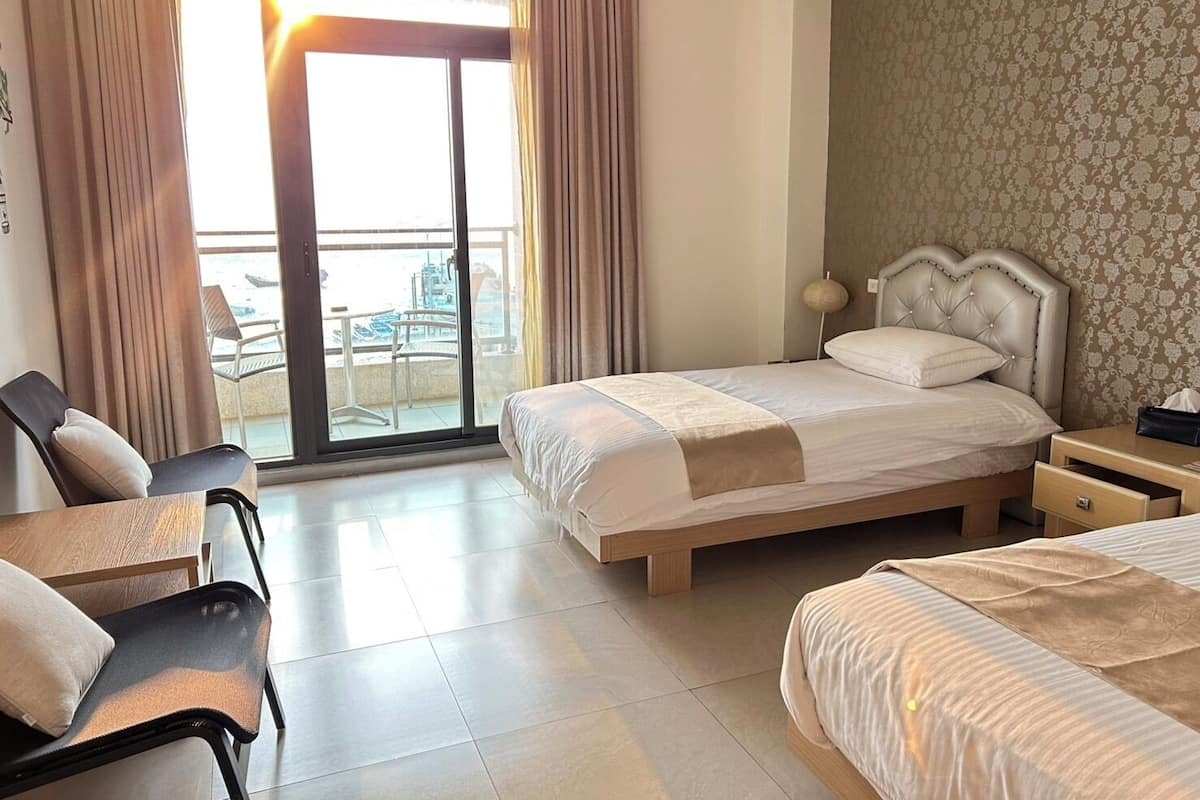 A hotel room with a bed, a desk, and a chair. There is a balcony with a view.