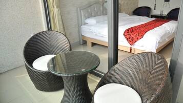 Un balcón con mobiliario de mimbre y una mesa de vidrio, un dormitorio con una cama y una manta roja, y una pared decorada con arte mural.