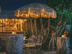 An outdoor bar area with a thatched umbrella, wooden furniture, and a bar stocked with bottles. - Rustico - a rustic vacation home surrounded by nature (Überlingen, Baden-Württemberg, Germany)