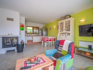 Un soggiorno con camino, una zona pranzo con tavolo e sedie, una cucina con pensili e un televisore.