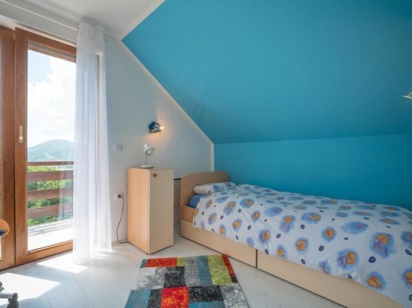 Un dormitorio con cama, mesita de noche, lámpara, ventana con cortinas y vistas al exterior.