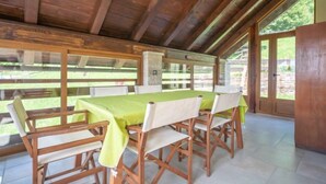 A covered outdoor dining area with a table and chairs, wooden beams, and large windows. - Lady Lavender by Interhome (Mrkopalj)