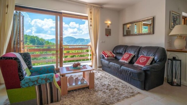 A living room with a sofa, a colorful chair, a small table, and a view of greenery and mountains through large windows. - Lady Lavender by Interhome (Mrkopalj)