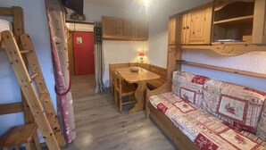 Una habitación acogedora con una mesa de madera, un banco, un televisor y una puerta roja.