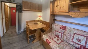 Cocina compacta con armarios de madera, una mesa de comedor y un sofá con cojines estampados.