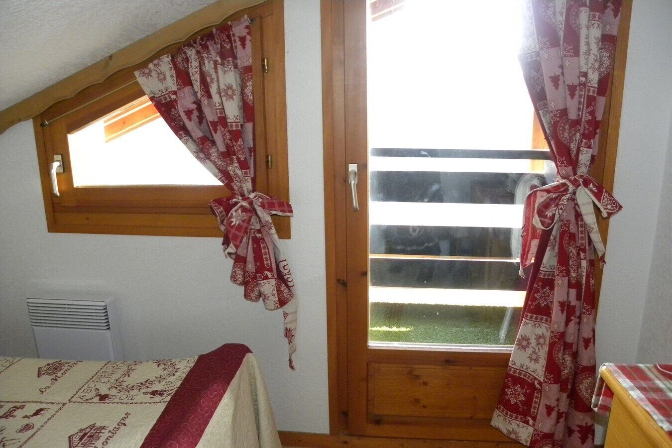 A room with a window, a door, and a bed with a patterned bedspread.