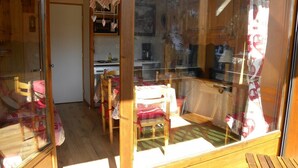 A cozy room with a wooden table and chairs, a small kitchen area, and a view of a building through a glass door. - P4 Duplex BELLECOMBE area of DIAMOND SPACE (Notre-Dame-De-Bellecombe)