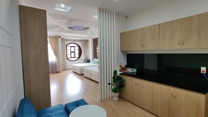 A modern hotel room with a sofa, a small round table, a kitchen area with wooden cabinets, a dining table, and a large window with curtains. - Winter Spring Homestay Center (Can Tho)