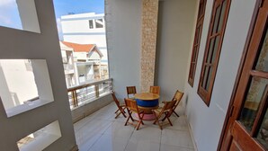 A balcony with a round table and chairs, a stone pillar, and a view of neighboring buildings. - Winter Spring Homestay Center (Can Tho)