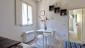 Quarto moderno e bem iluminado, com mesa de jantar, cadeiras, radiador e janela.