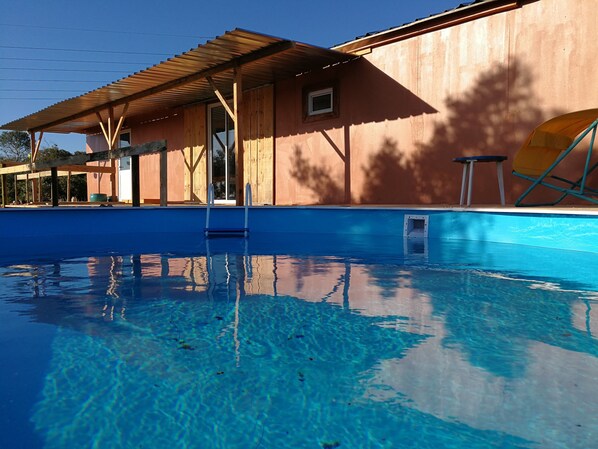 En swimmingpool med træterrasse og en bygning i baggrunden.