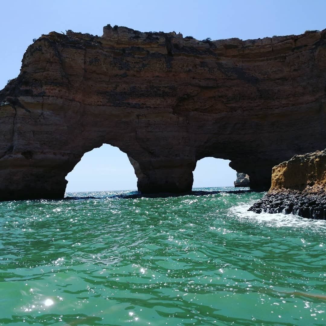 Une formation rocheuse naturelle avec deux arches se dressant au-dessus d’une eau d’un bleu cristallin.