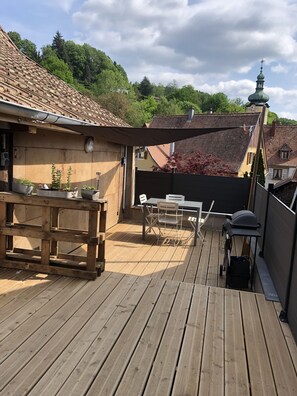 A wooden deck with a table and chairs, potted plants, and a barbecue grill. - Vintage apartment in the old forge (Muhlbach-sur-Munster)
