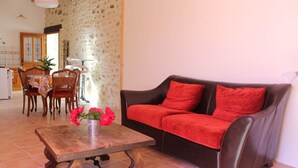 A living room with a brown leather sofa, a wooden coffee table with a vase of red flowers, and a dining area with wooden chairs and a table. - Apartment in a quiet village house (Colonzelle)