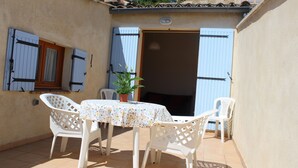 An outdoor patio with a round table and four white chairs, a potted plant, and a door with blue shutters. - Apartment in a quiet village house (Colonzelle)