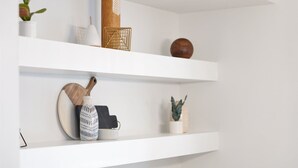 A white wall with three shelves holding various decorative items, a white cabinet with gold handles, and a marble countertop. - Bright 3BR · 5 Mi to Disneyland · Sleeps 8, 2 BA (Fullerton)