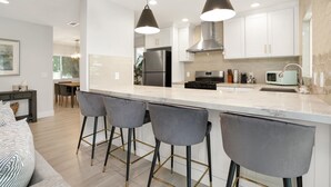 A modern kitchen with a central island, bar stools, stainless steel appliances, and pendant lighting. - Bright 3BR · 5 Mi to Disneyland · Sleeps 8, 2 BA (Fullerton)