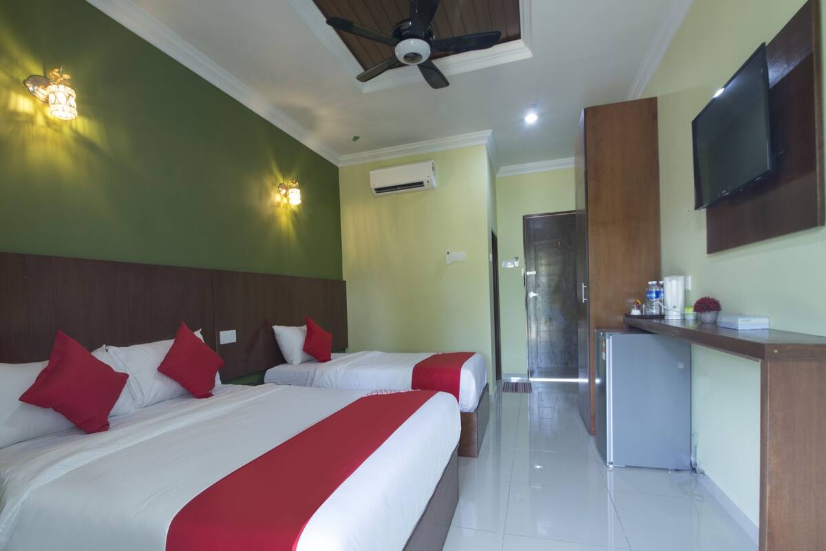Ein Hotelzimmer mit zwei Betten, einem Deckenventilator, einer Klimaanlage, einem Fernseher und einer kleinen Küchenzeile.