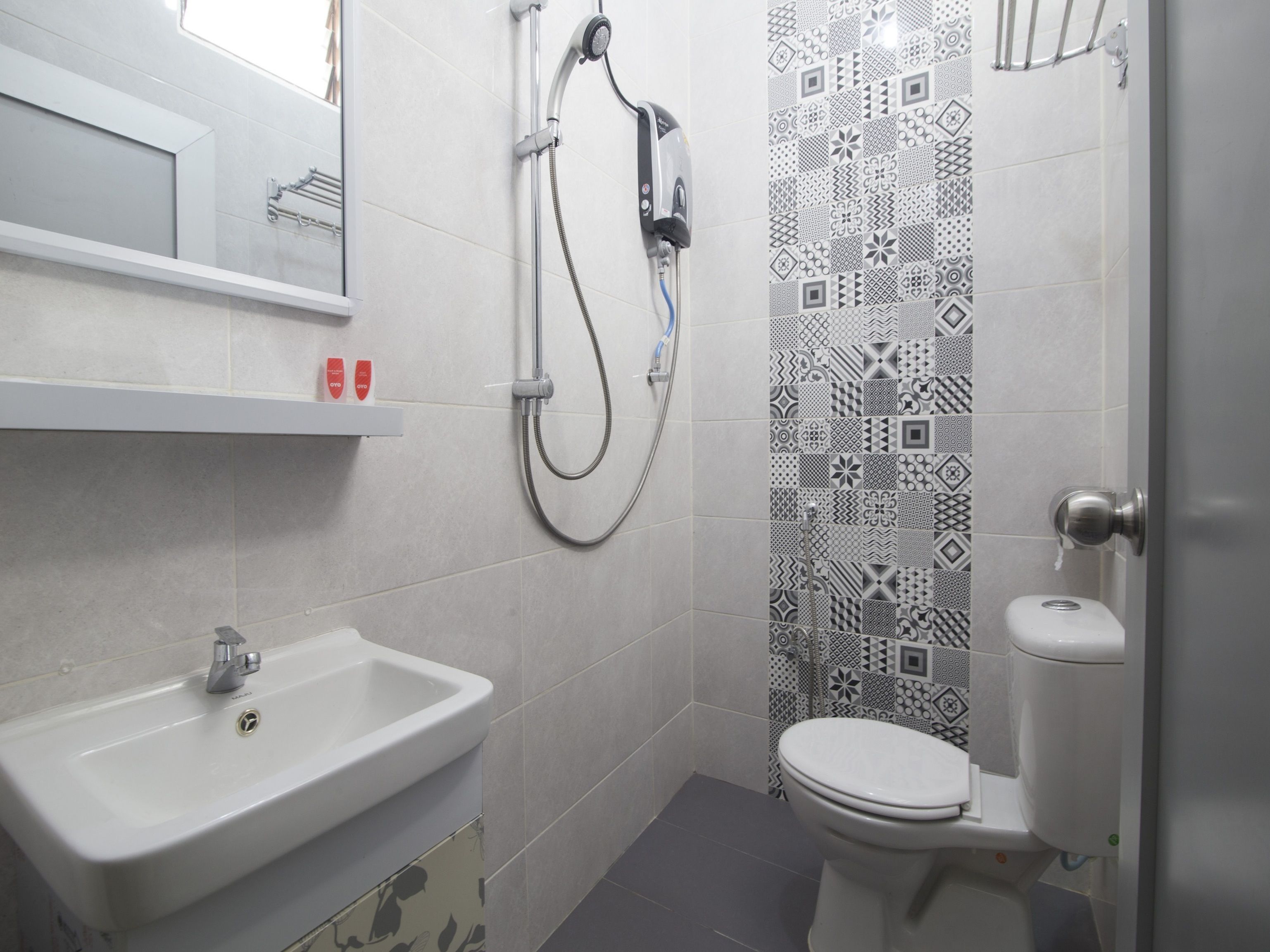 Un baño con lavamanos blanco, inodoro y ducha con pared de azulejos estampados.