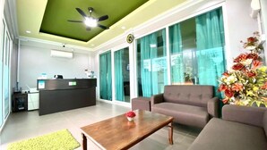 A reception area with a reception desk, a sofa, a coffee table, and a large window with curtains. - Norshah Village Resort (Langkawi)